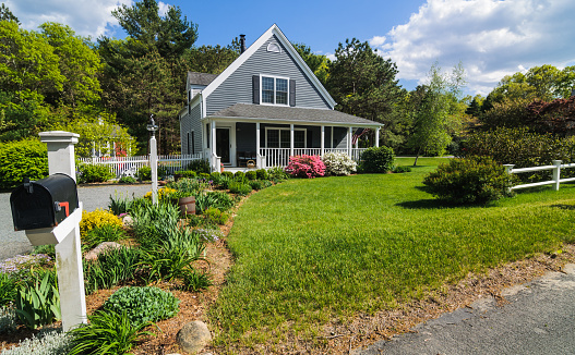 An American flag flies from the open porch and gardens surround a small  single family home on a Spring afternoon on Cape Cod on the Massachusetts coast.c (Property Release Attached)