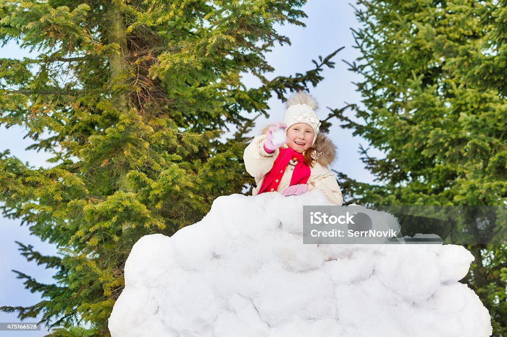 Beautiful small girl holds snowball in the forest Beautiful small girl holds snowball and stands behind the snow wall with forest on the background 2015 Stock Photo