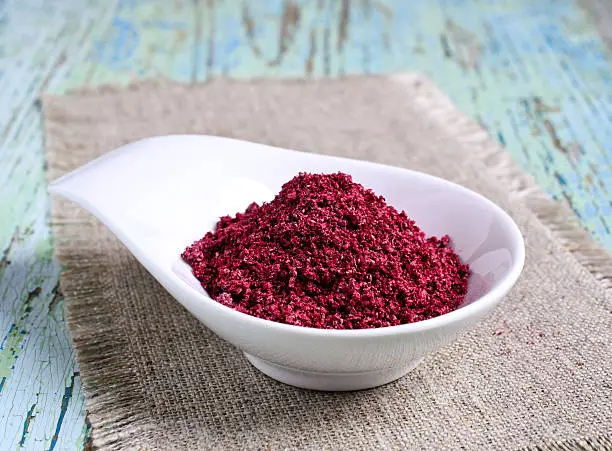 Ground sumac in ceramic bowl on wooden surface