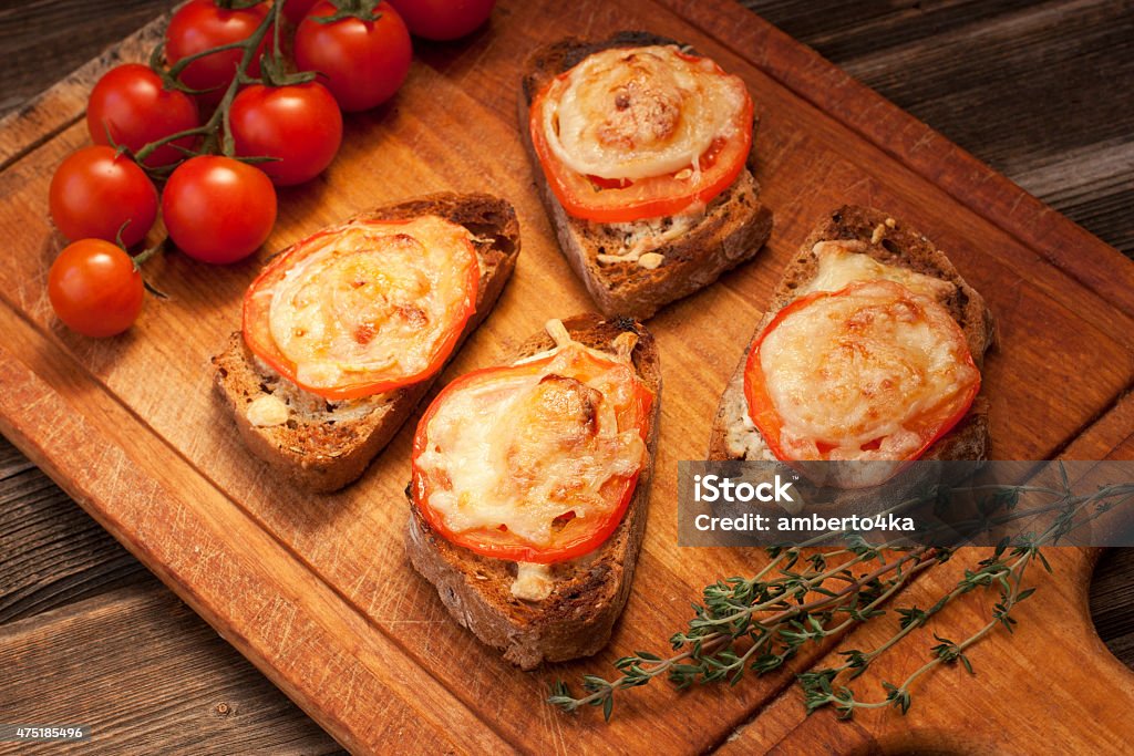 Delicious bruschetta with tomatoes on cutting board Bruschetta with roasted tomatoes, cheese and herbs 2015 Stock Photo
