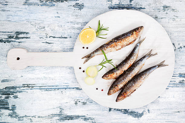 Grilled sardines. Delicious grilled sardines on wooden kitchen board on white and blue wooden textured background. Culinary seafood eating. sardine photos stock pictures, royalty-free photos & images