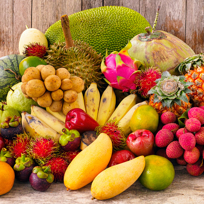 A wide selection of well-known, famous market fresh tropical Thai fruit on an old wooden table. The selection includes Durian, Jackfruit, Coconut, Mangosteen, Lynchee/Lychee, Rose Apple, Longan, Mango, Pineapple, Guava, Pineapple, Rambutan, Thai Orange, tangerine, Thai Bananas, Dragon fruit and Watermelon.