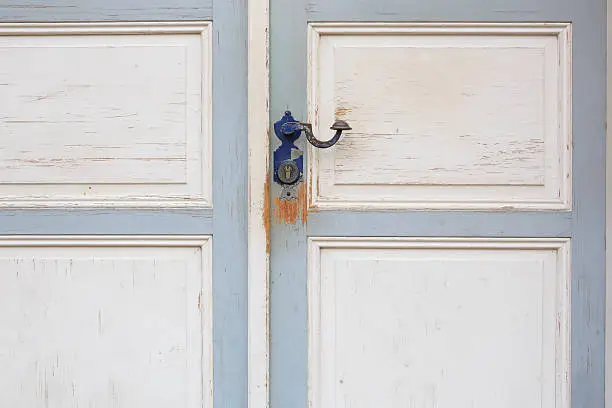 Two-wing door with blue door handle in full frame detail view. Area below keyhole is scratched and raw wood visible. Door painted blue and white.