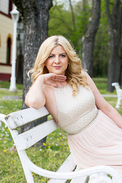Blond woman in evening gown sitting on white bench