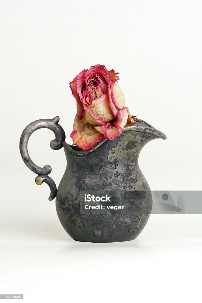 Dried rose in a vintage jug A dried rosebud in nicely designed very old creamer calls to mind the fugacity of time and revives old memories, may illustrate marriage years or sentimental past Attitude Stock Photo