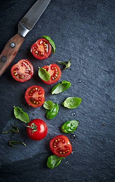 istock Halved cherry tomatoes and basil leaves on black slate 475219130