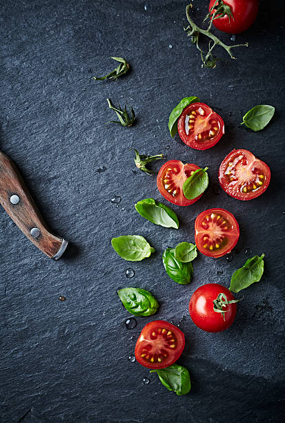 Halved cherry tomatoes and basil leaves on black slate