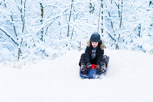 маленький мальчик, наслаждаясь катание на санях в snowy forest - little boys sled clothing slide стоковые фото и изображения
