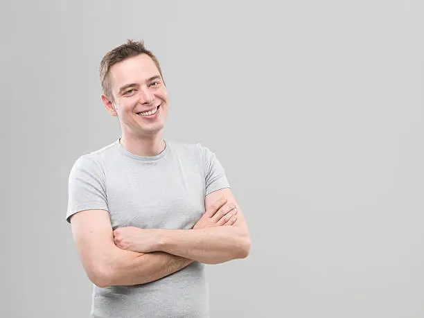 happy caucasian man standing with crossed arms against his chest, on grey background. copy space available