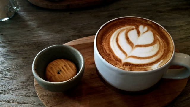 cup of coffee latte with biscuit on tray wood