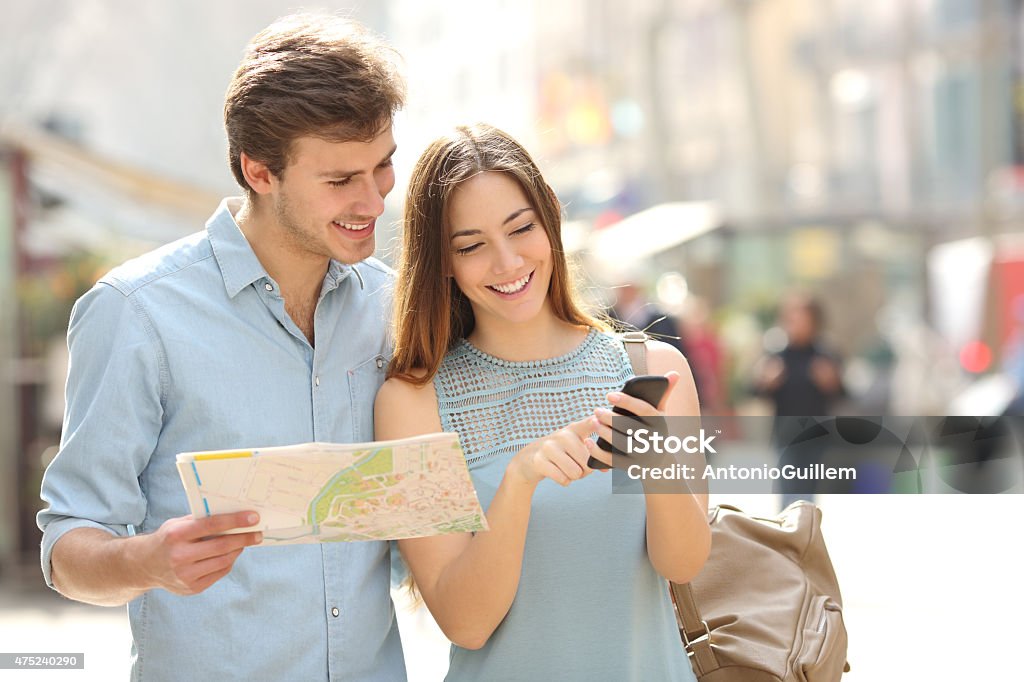 Couple of tourists consulting a city guide and smartphone gps Couple of tourists consulting a city guide and smartphone gps in the street searching locations Tourist Stock Photo