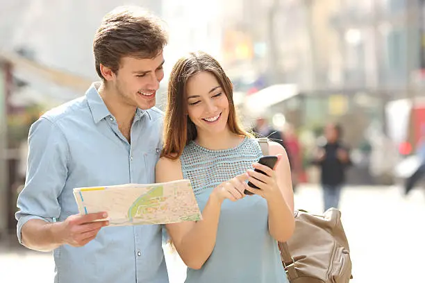 Photo of Couple of tourists consulting a city guide and smartphone gps