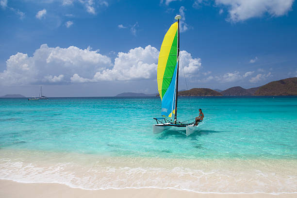 bikini woman sailing on a catamaran toward the Caribbean beach young woman in bikini sailing on a catamaran toward the Virgin Islands white sand beach catamaran sailing stock pictures, royalty-free photos & images