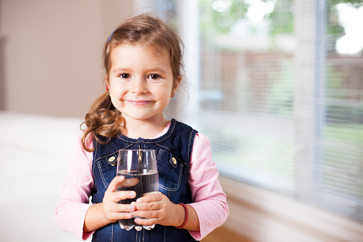 Little girl holding a water glass, looking at the camera
