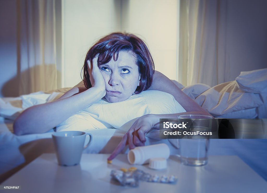 red haired woman sick in bed with medicine red haired woman sick with flu or cold in bed with water and medicine in the foreground Alcohol - Drink Stock Photo