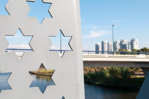 Star of Davids are designed into a bridge spanning the HaYarkon River in Tel Aviv, Israel. Apartment/office buildings are in the distance.