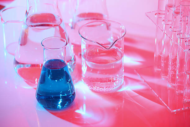 Science research laboratory background, with glass chemistry equipment, beakers, test tubes, flask filled up with blue liquid. Light red background.