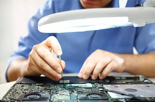 Photo of Man unscrewing motherboard of a laptop.