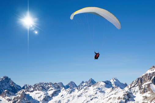 two people paragliding in tandem high in the blue sky