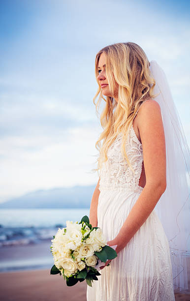 istock beautiful bride standing by the beach at sunset 475254217