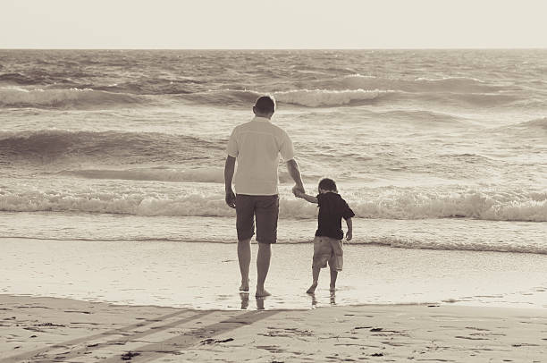 istock happy father and little son walking together on beach sunset 475257362
