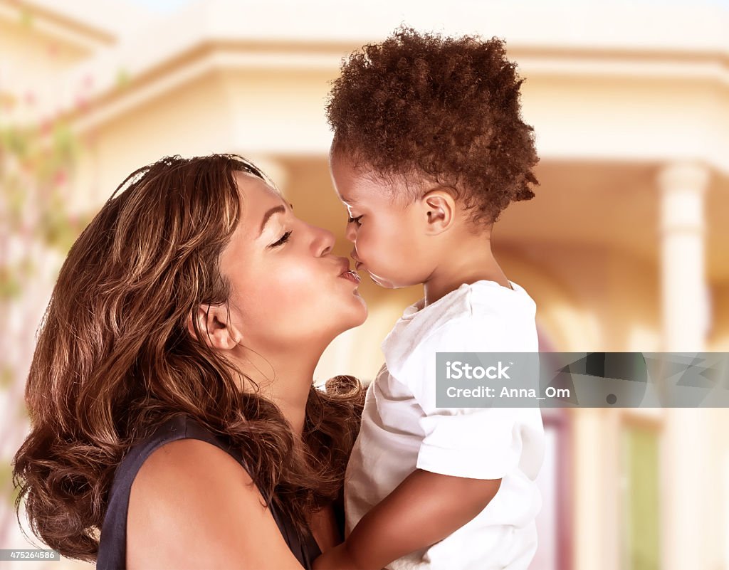 Happy mother with cute son Side view of cheerful mother holding on hands cute little curly son and kiss him, spending time outdoors near great beautiful house, happy African family Mother Stock Photo