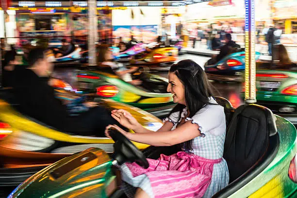 Beautiful girl in an electric bumper car in amusement park in typical German Dirndl dress with bright colours and lights in the background