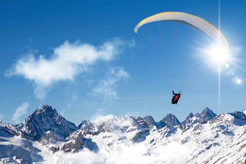 two people paragliding in tandem high in the blue sky