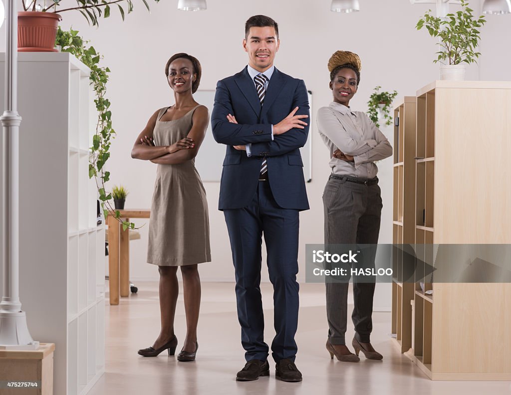 Team leader stands with coworkers in background Team leader stands with coworkers in background. Multi ethnic group of people 2015 Stock Photo