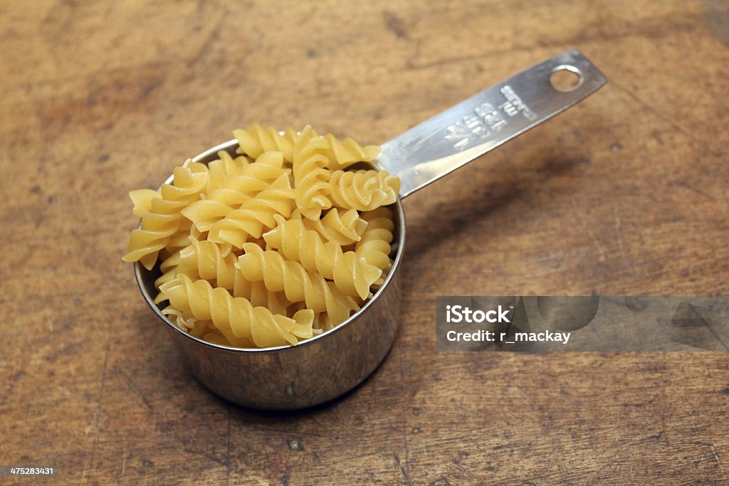 Pasta in measuring cup Measuring cup fill of sprial pasta over wood background Baking Stock Photo