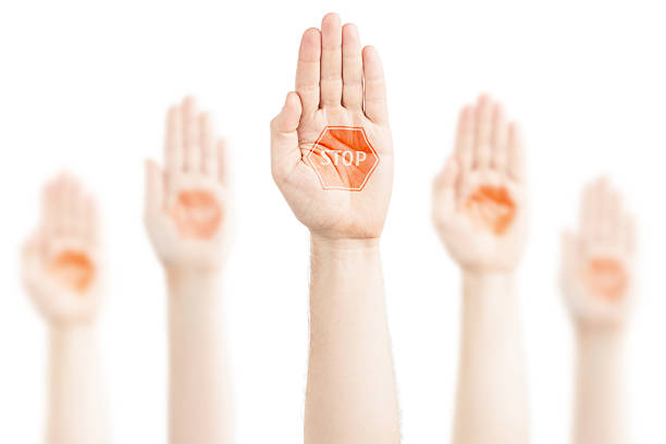 A dark-skinned man's hand is held up, palm forward in a stopping gesture.
