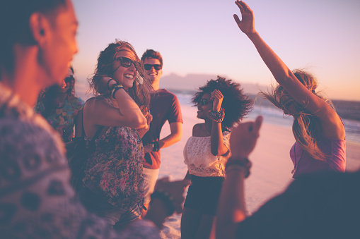 Group of friends dancing on the beach at a sunset beachparty on a summer evening
