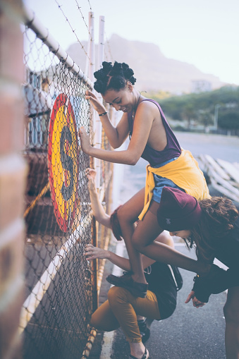 Mixed race friends helping an Afro grunge girl climb up an urban fence