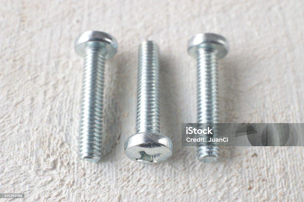 Three screws on a white wooden table. 3 screws placed parallel on a white wooden table. 2015 Stock Photo