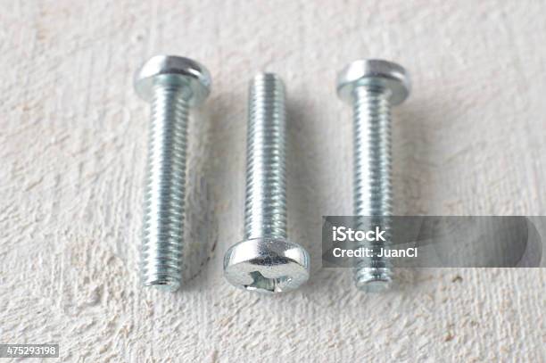 Three Screws On A White Wooden Table Stock Photo - Download Image Now - 2015, Bolt - Fastener, Chrome