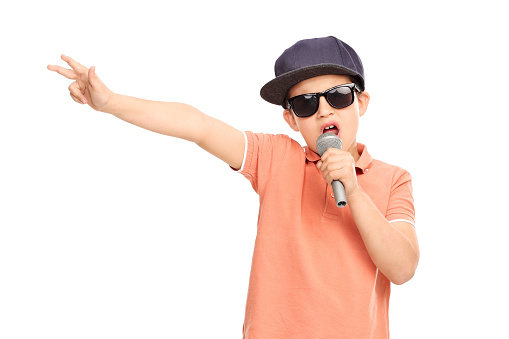 Little boy in hip hop outfit rapping on a microphone and gesturing with his hand isolated on white background