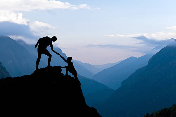 Teamwork couple climbing helping hand Teamwork couple helping hand trust assistance silhouette in mountains, sunset. Team of climbers man and woman hiker, help each other on top of mountain, climbing assistance, beautiful sunset landscape in Himalayas Nepal rock climbing stock pictures, royalty-free photos & images