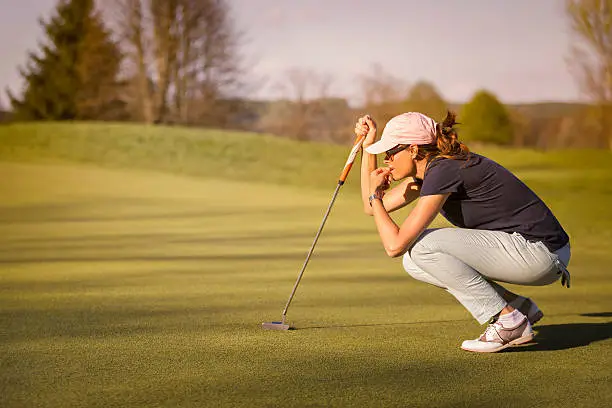 Woman golf player crouching and study the green before putting shot.