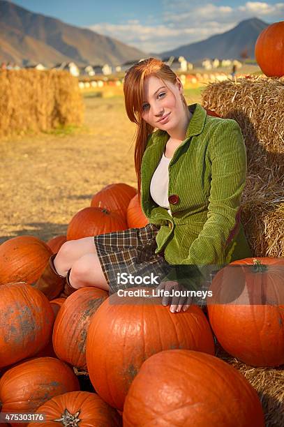 Red Headed Young Woman Sitting On A Pile Of Pumpkins Stock Photo - Download Image Now