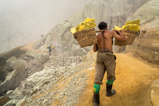 In East Java island in Indonesia, the volcano Kawah Ijen contains plenty of natural sulfur. Indonesian male workers carry the blocks of sulfur in two baskets on their shoulder and they have to climb the crater to the top and down to the village.