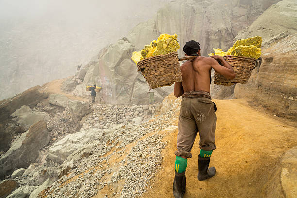 Asian worker carrying baskets of sulfur in Ijen volcano In East Java island in Indonesia, the volcano Kawah Ijen contains plenty of natural sulfur. Indonesian male workers carry the blocks of sulfur in two baskets on their shoulder and they have to climb the crater to the top and down to the village. fumarole photos stock pictures, royalty-free photos & images