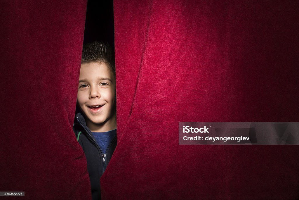 Child appearing beneath the curtain Child appearing beneath the curtain. Red curtain. Appearance Stock Photo