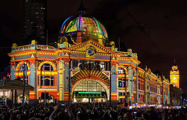 White Night Melbourne - Flinders St Station Melbourne, Australia - February 22, 2014: Large crowds gather outside Flinders Street Station, as a design inspired by Luna Park is projected onto its facade as part of White Night Melbourne, an all-night arts festival. melbourne street crowd stock pictures, royalty-free photos & images