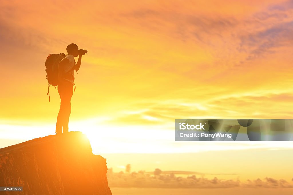 Success man on the mountain Silhouette of a Success man mountain climber stand on top of mountain and look sunshine Binoculars Stock Photo