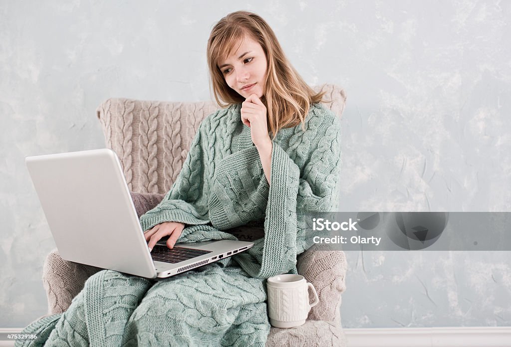 Woman working at home using laptop Attractive woman with natural blond hair posing without makeup with working at home using laptop, sitting in cute armchair with cup of hot drink 2015 Stock Photo