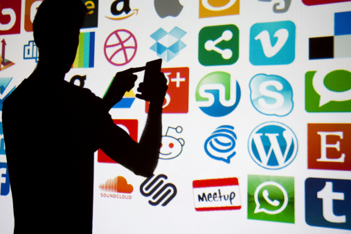 London, United Kingdom - February 17, 2014: A silhouetted smartphone being used in front of social media and technology logos. Logos include vimeo, wordpress, whatsapp, meetup,