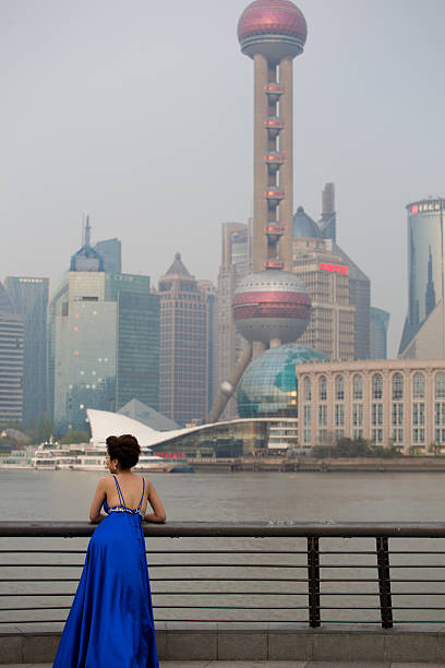 China, Shanghai, April 8, 2013: Beautiful unrecognizable girl dressed in a blue dress on the Bund, in front of The most famous landmark in Shanghai, The Oriental Pearl Tower.