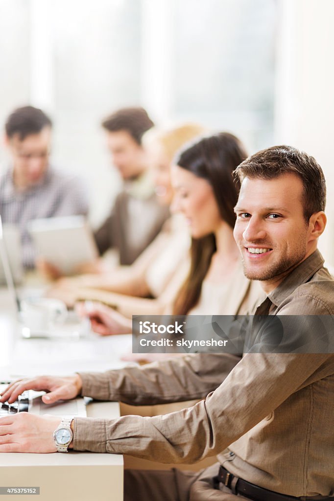Smiling young businessman on a meeting looking at camera. Business people having a business meeting in the office. Focus is on foreground, on a happy businessman looking at the camera. 2015 Stock Photo