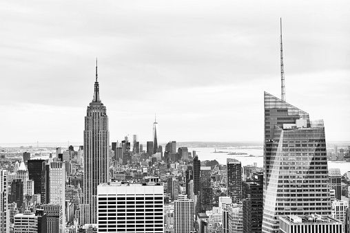 This is a horizontal, black and white, royalty free stock photograph of the New York City skyline viewed from Brooklyn. Manhattan buildings fill the lower part of the frame. A clear sky gives copy space. The iconic, landmark architecture, the Empire State Building stands taller than the other urban city structures. Photographed with a Nikon D800 DSLR camera.