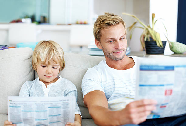 istock Dad and son reading newspapers together on couch. 475383323